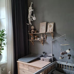 Above a changing table in a nursery with a grey wall, a white Clérachic monkey wall light hangs high with its bulb dangling.