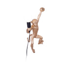 A gold Clérachic monkey wall light on a plain white backdrop, one arm gripping the top, with a black socket and white globe.