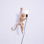 Gold monkey of this Clérachic wall light shown side-on on a lilac-white wall, its tail curled out and a black cord falling below.