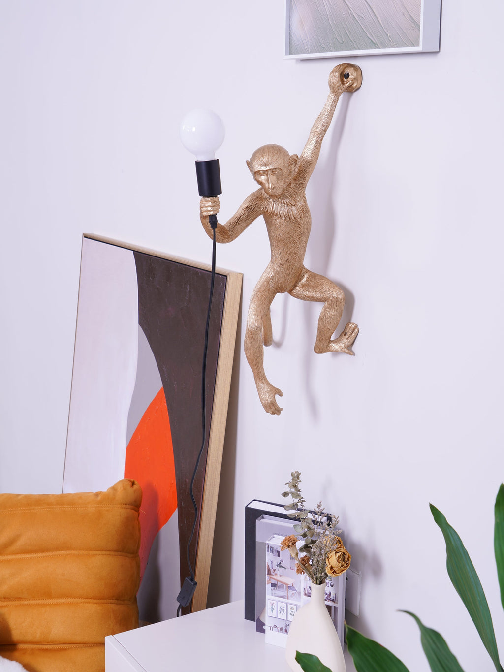 Gold monkey wall light from Clérachic, reaching up with one arm, with a large artwork and orange seat close below.