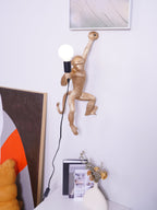 This Clérachic monkey wall light in gold looks down from a white wall, a vase of dried stems on the cabinet beneath it.