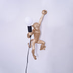 Close view of the gold monkey on this Clérachic wall light, its large white globe bulb held in a black socket.