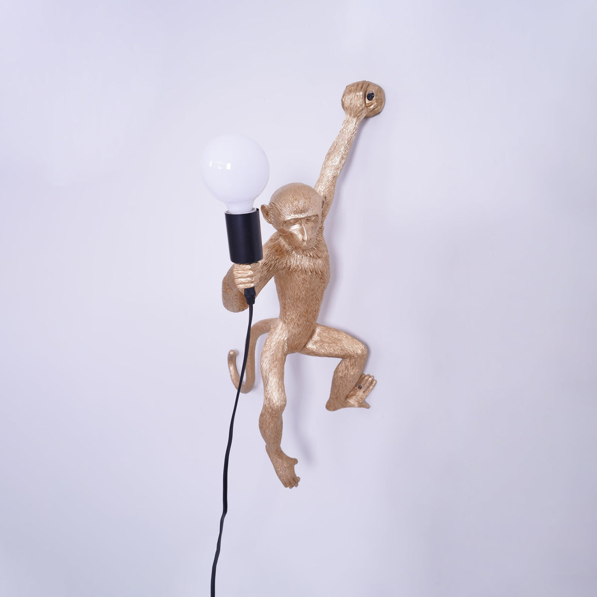 Close view of the gold monkey on this Clérachic wall light, its large white globe bulb held in a black socket.