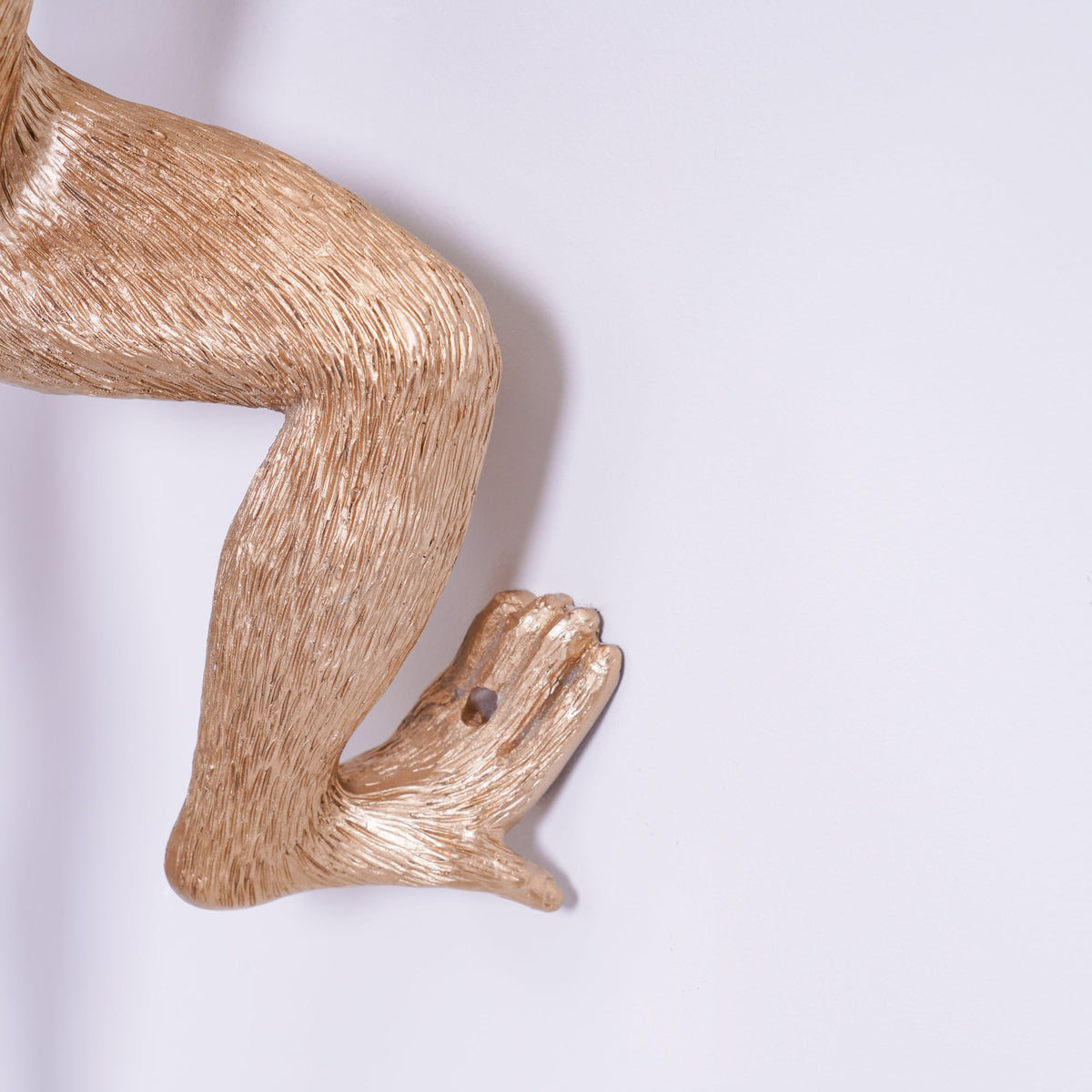 Close view of the gold monkey's bent leg and foot on this Clérachic wall light, showing the fine fur texture in the resin.