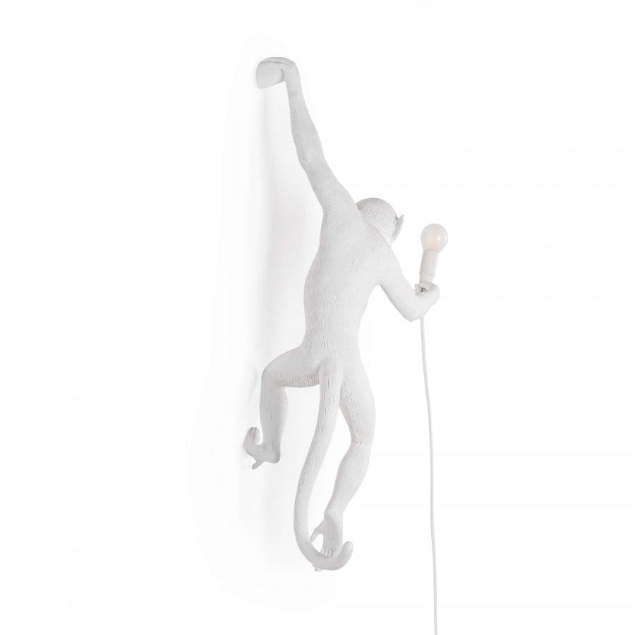A white Clérachic monkey light almost vanishes into a white backdrop, one arm up, with a small bulb held out to the right.