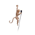 A gold Clérachic monkey light with its tail curled to the left, holding a black socket and bulb against a white background.