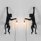 A pair of black Clérachic monkey wall lights face each other, one left and one right, their bulbs casting a warm glow between.