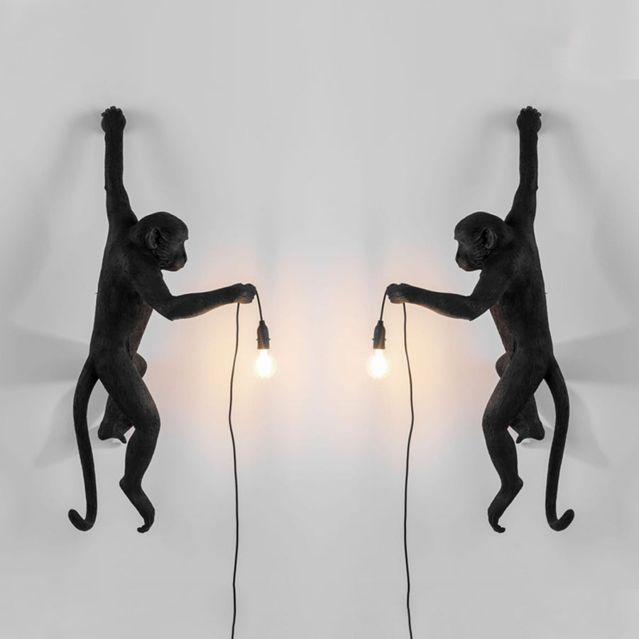 A pair of black Clérachic monkey wall lights face each other, one left and one right, their bulbs casting a warm glow between.