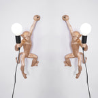A pair of gold Clérachic monkey wall lights, left and right mirrored, each holding a white globe bulb on a pale grey wall.