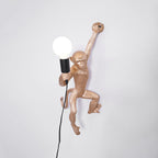 Gold monkey wall light from Clérachic with its globe bulb on the left, set on a pale grey wall with a black cord below.