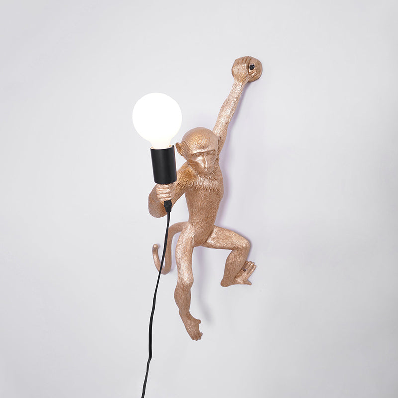 Gold monkey wall light from Clérachic with its globe bulb on the left, set on a pale grey wall with a black cord below.