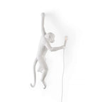 A white Clérachic monkey wall light on a white backdrop, its raised arm and long tail leaving a faint shadow on the wall.