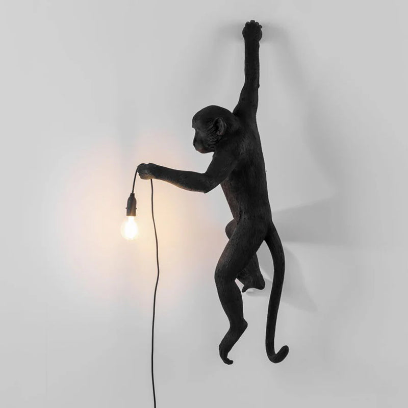 The black version of this Clérachic monkey light, facing left, holds a filament bulb that lights the wall beside it.