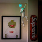 This Clérachic monkey wall light holds a blue-tinted bulb in a dim room, next to a framed frog portrait and a red skateboard.