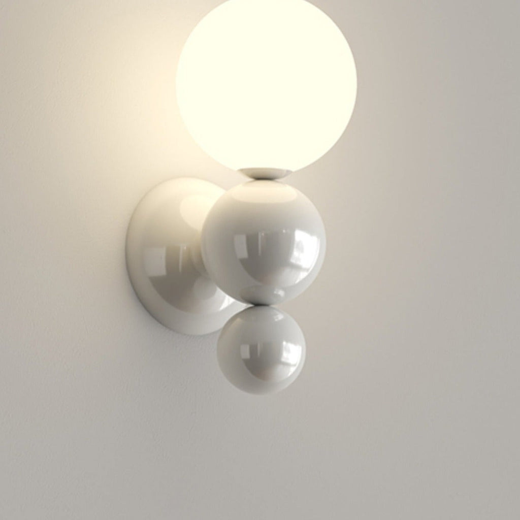 The Clérachic three-sphere wall light in white, its lit opal globe stacked above two glossy white spheres on the wall.