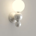 The Clérachic three-sphere wall light in white, its lit opal globe stacked above two glossy white spheres on the wall.