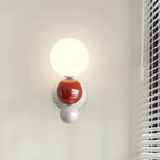 The Clérachic three-sphere wall light in red, a glossy red sphere between the lit opal globe and a white base sphere, beside window blinds.