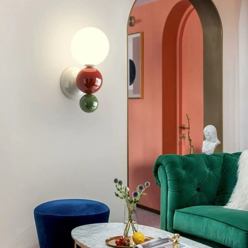 The Clérachic three-sphere wall light in green, lighting a coral archway beside a green velvet sofa and a plaster bust.