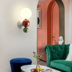 The Clérachic three-sphere wall light in green, lighting a coral archway beside a green velvet sofa and a plaster bust.