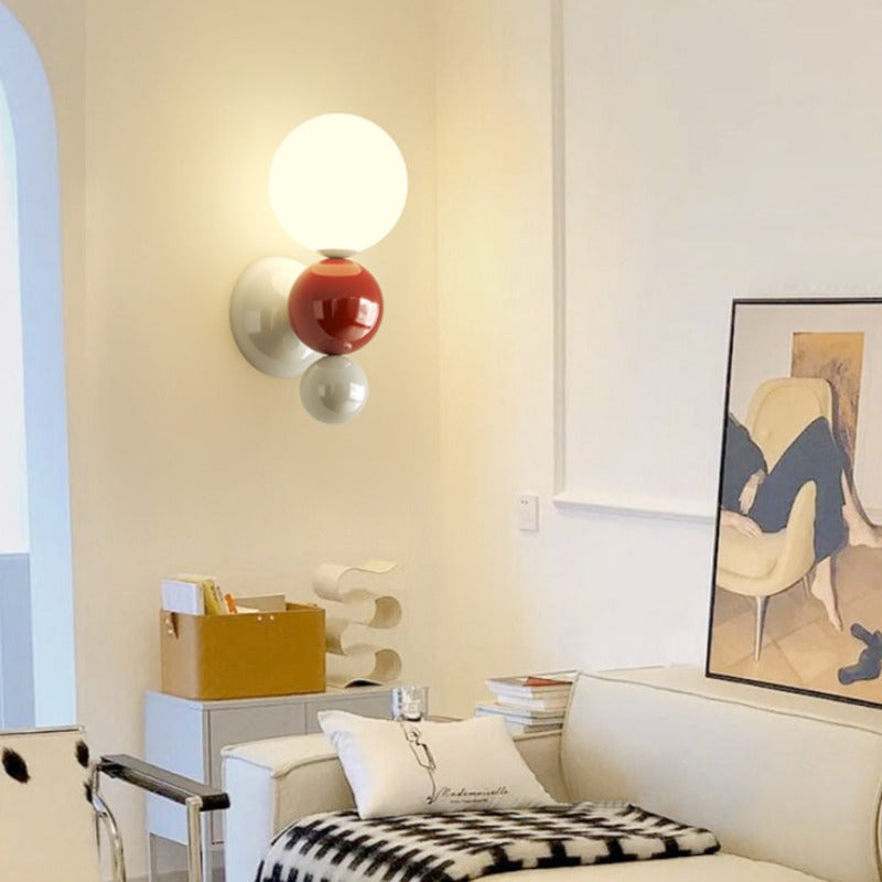 The Clérachic three-sphere wall light in red, glowing beside a cream sofa and framed art print in a living room.