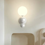 The Clérachic three-sphere wall light in white, glowing above a curved headboard nook in a bedroom.