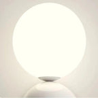 Close-up of the Clérachic three-sphere wall light's lit opal glass globe glowing against a plain wall.