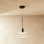 Clérachic two-tier pendant with a shallow white disc over a wider one on a black stem, against a limewash wall.