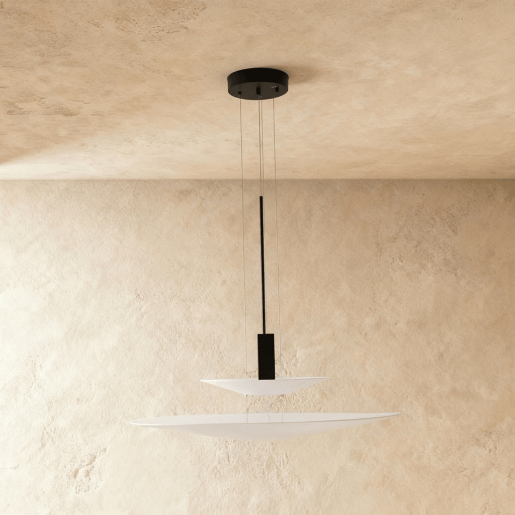 Clérachic pendant with two stacked white frosted discs and a black weight on thin wires, on a limewash backdrop.