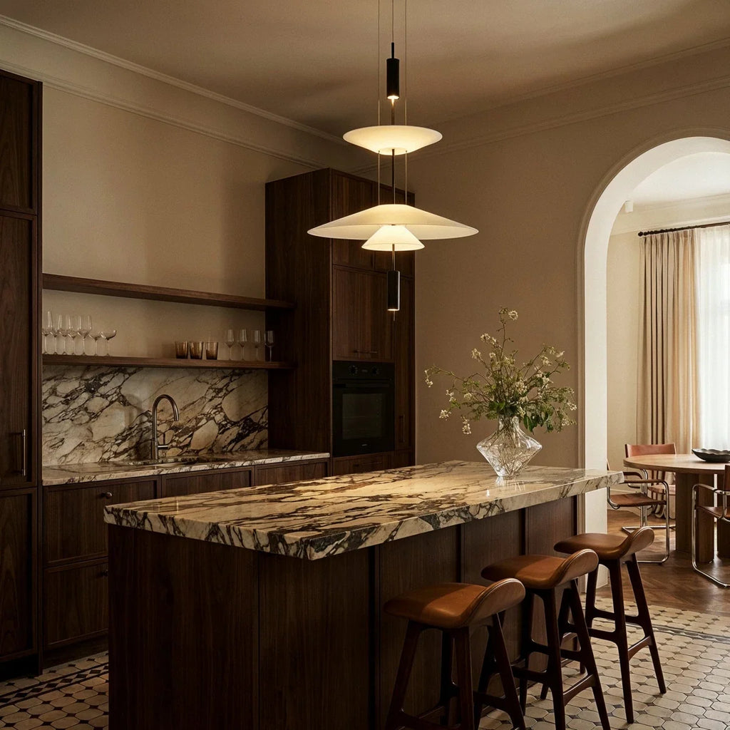 Clérachic tiered white pendant glowing above a marble-topped kitchen island with leather stools and dark wood cabinets.