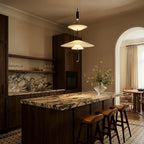 Clérachic tiered white pendant glowing above a marble-topped kitchen island with leather stools and dark wood cabinets.