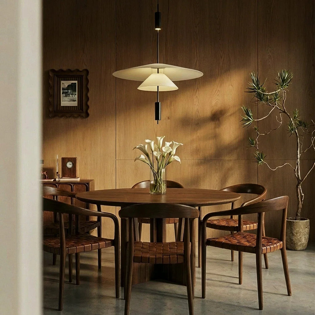 Clérachic white tiered pendant hung over a round walnut dining table with woven leather chairs and calla lilies.