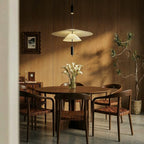 Clérachic white tiered pendant hung over a round walnut dining table with woven leather chairs and calla lilies.