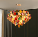 Clérachic agate chandelier lit against a dark wall and grey curtain, its stone slices glowing red, green and amber.