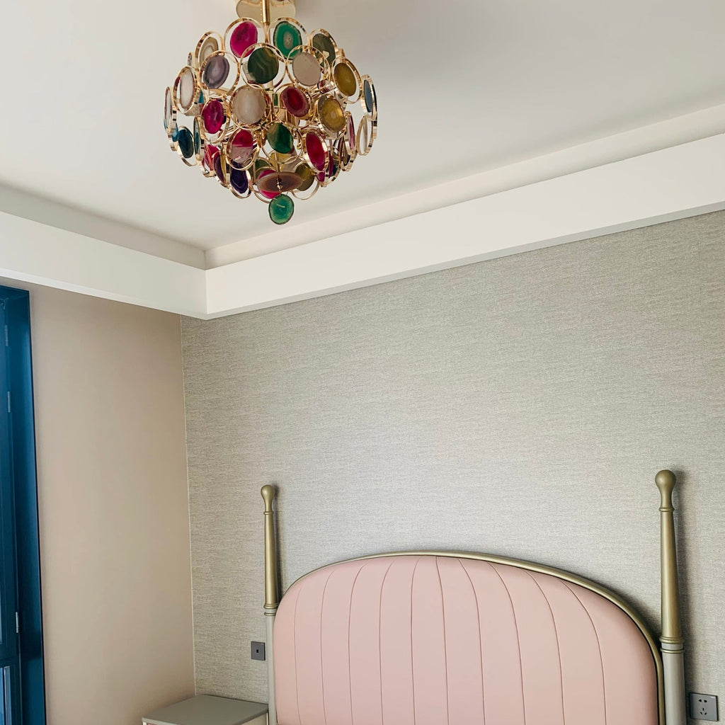 A Clérachic agate chandelier mounted high on a white ceiling above a pink bed headboard, seen from across the room.