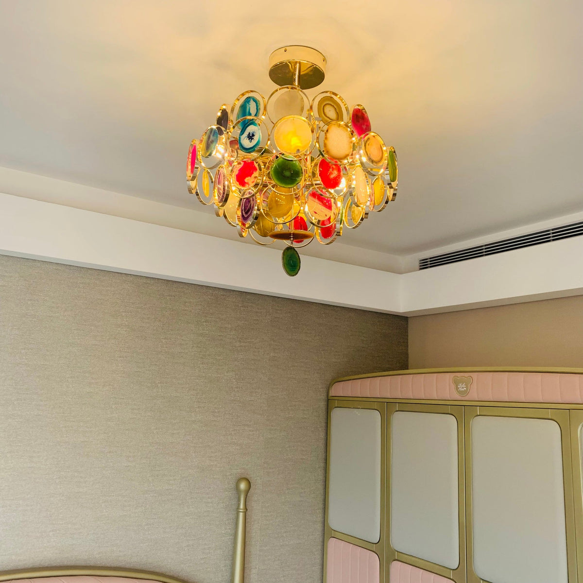 Clérachic agate chandelier lit close to the ceiling of a room with a pink wardrobe, casting a warm glow upwards.