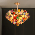 Clérachic agate chandelier lit in front of a dark panelled wall, with a hanging amber slice at its base.