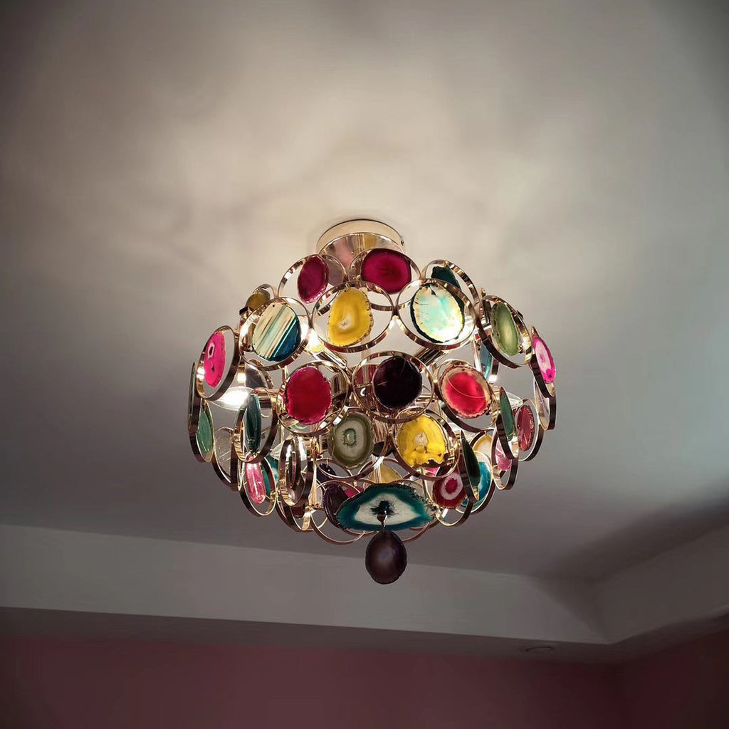 Looking up at a Clérachic agate chandelier on a grey ceiling, its stone slices in pink, teal and gold catching the light.
