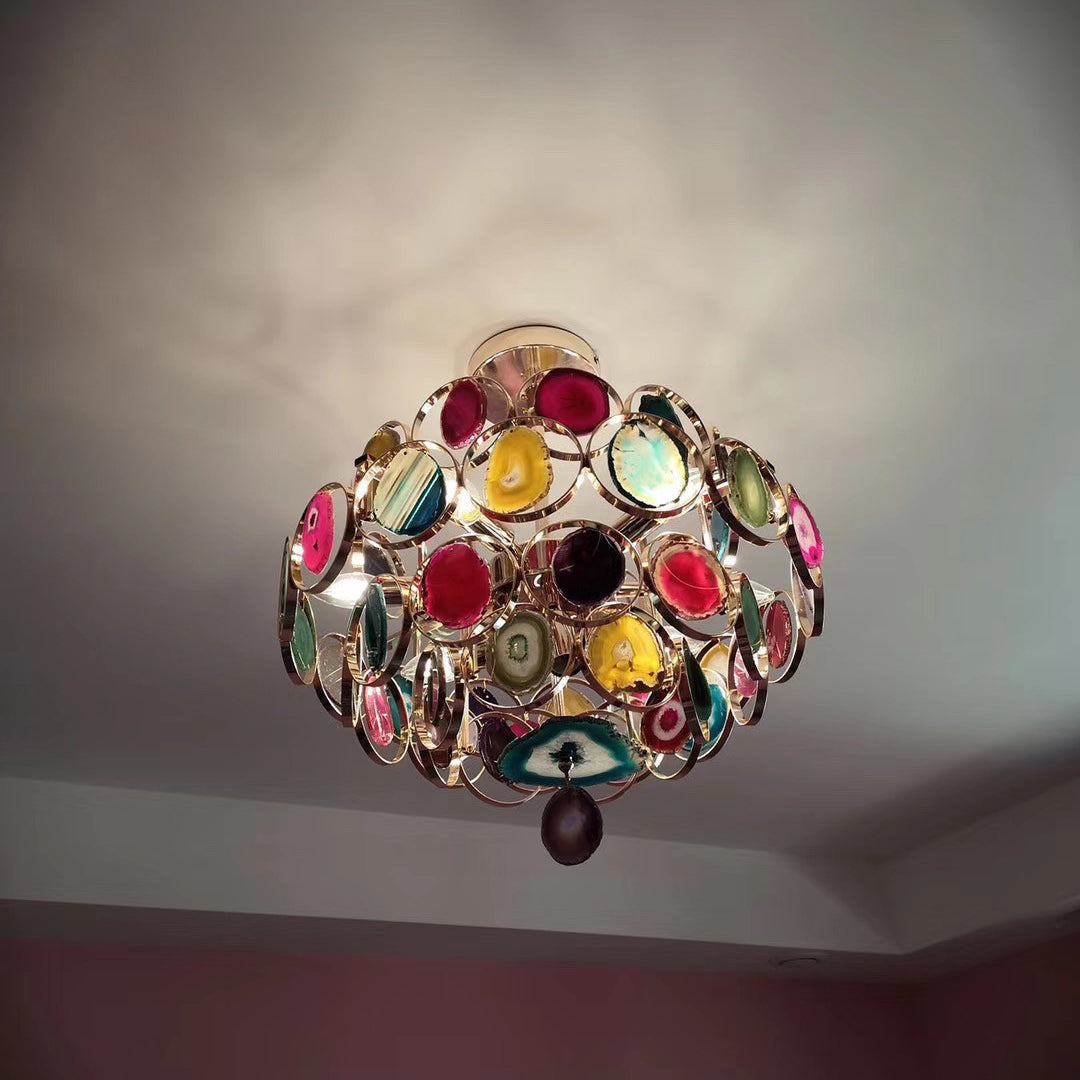 Looking up at a Clérachic agate chandelier on a grey ceiling, its stone slices in pink, teal and gold catching the light.