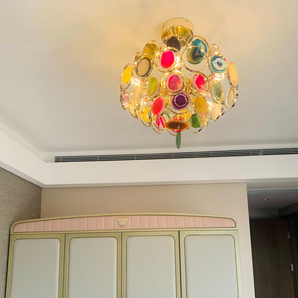 A compact Clérachic agate chandelier on a white ceiling, with a green slice hanging below and a pink wardrobe beneath.
