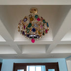 Looking up at a Clérachic agate chandelier in a coffered ceiling, with a pink slice hanging below and a doorway beyond.