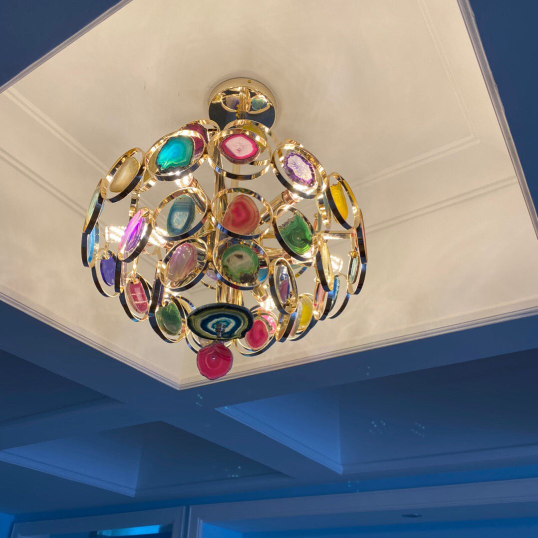A Clérachic agate chandelier set into a white coffered ceiling with a blue ceiling edge, its slices in pink, teal and gold.