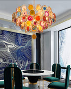 This Clérachic agate chandelier hangs above a round marble table with green chairs, near a blue patterned wall.
