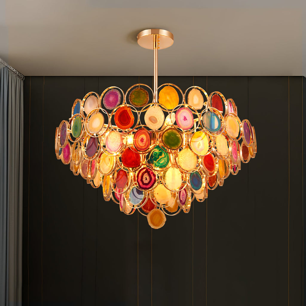 Clérachic agate chandelier lit on a dark green wall, its tiers of stone slices glowing warm at the centre.