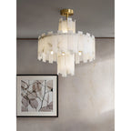 Clérachic Tiered Alabaster Chandelier lighting a plaster wall beside a framed botanical print in a warm-toned room.