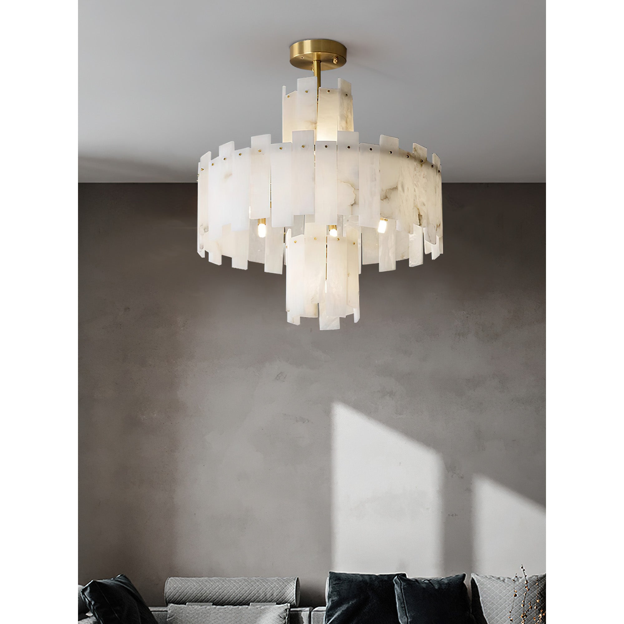 Clérachic Tiered Alabaster Chandelier over a grey seating area, daylight crossing the concrete wall behind it.