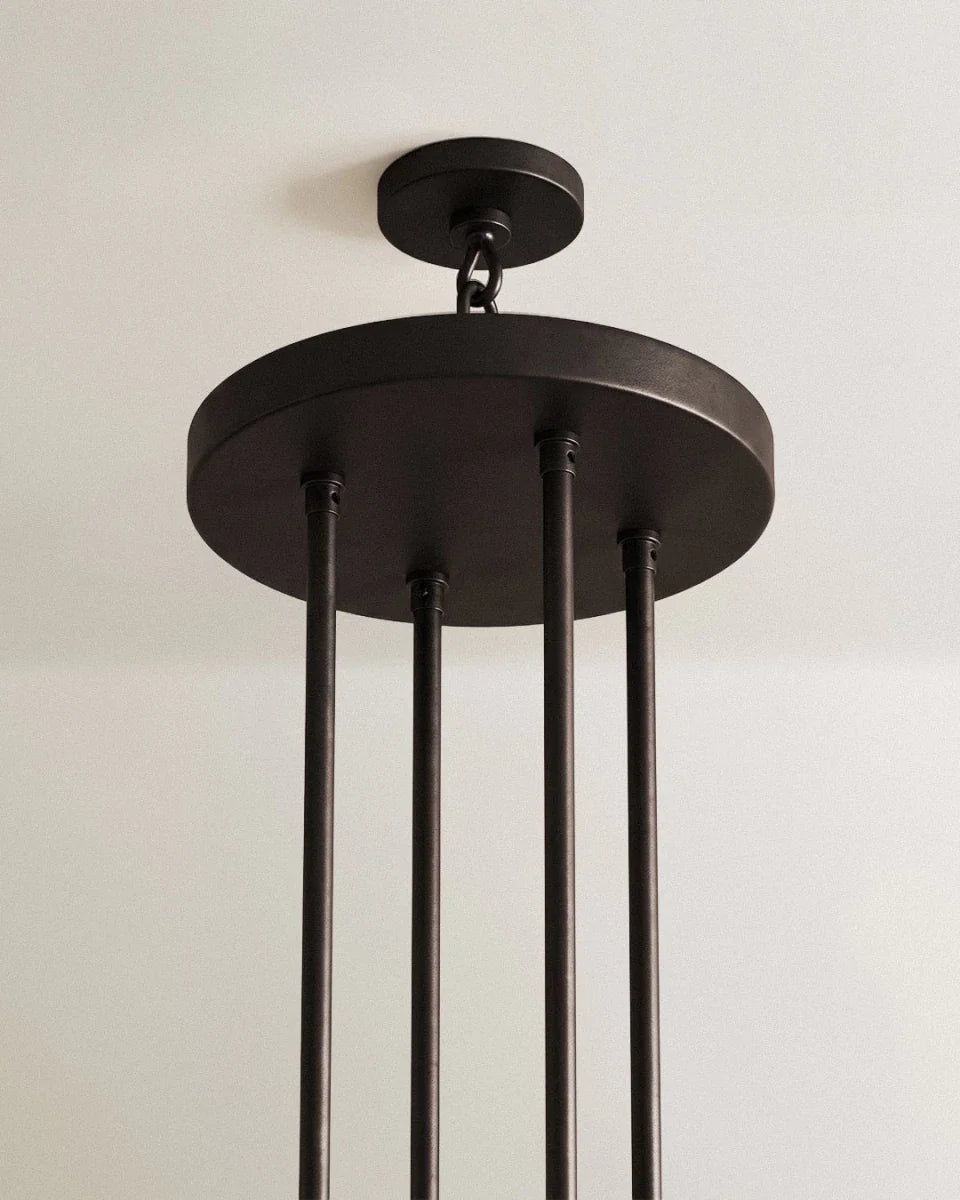 Close view of the matte black canopy and four slim rods of a Clérachic tiered chandelier, hung by a chain from a ceiling plate.