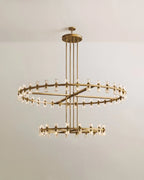 Clérachic two-tier chandelier in brushed lacquered brass, with glass cylinders around a wide upper ring and a smaller lower ring.