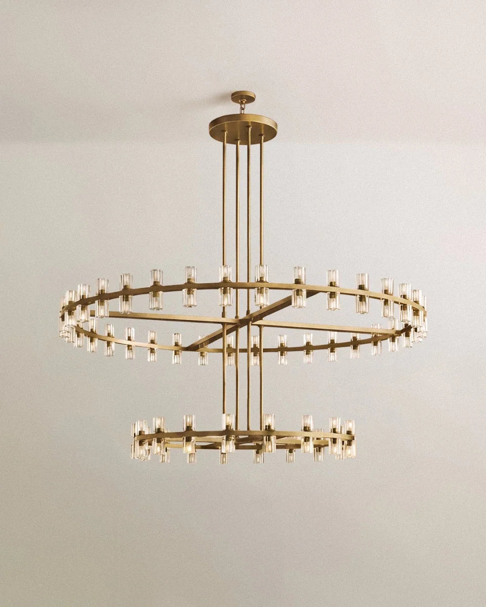 Clérachic two-tier chandelier in brushed lacquered brass, with glass cylinders around a wide upper ring and a smaller lower ring.