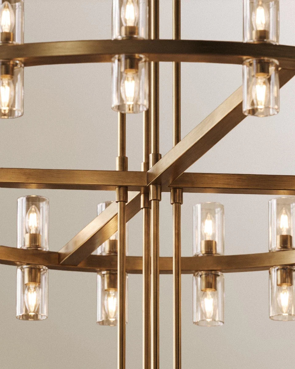 Close view of a Clérachic lacquered brass chandelier, showing clear glass cylinders, filament bulbs and the cross arms between rings.