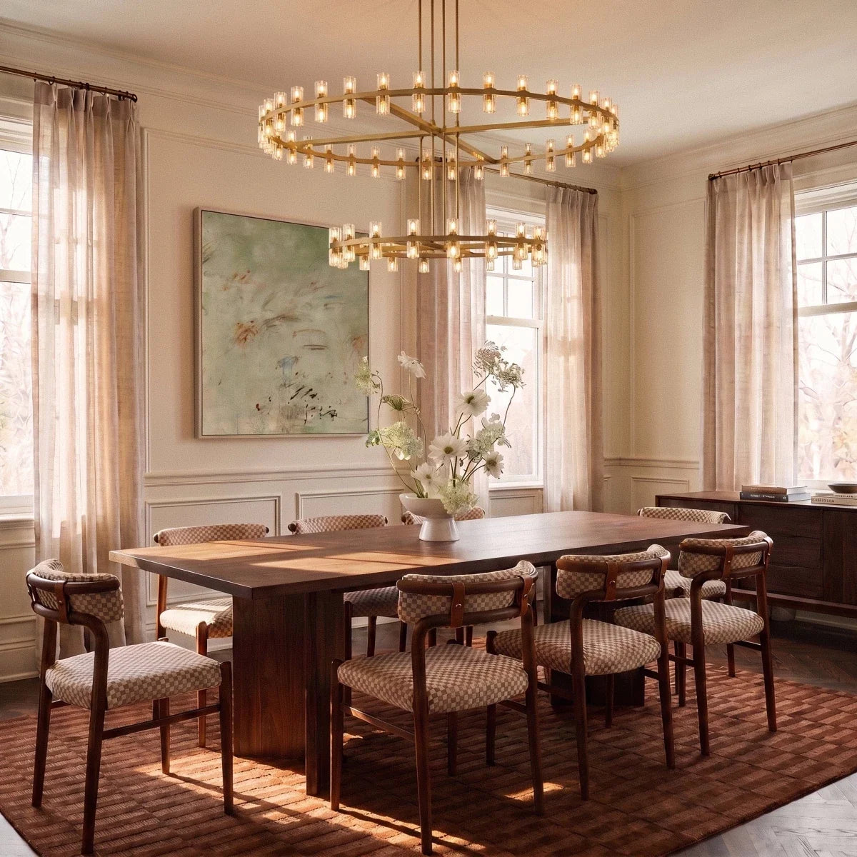 Clérachic lacquered brass tiered chandelier above a long walnut dining table with checked chairs and sheer curtains.